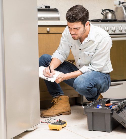 Portrait of a handsome male technician doing a work report on a broken fridge in a home kitchen